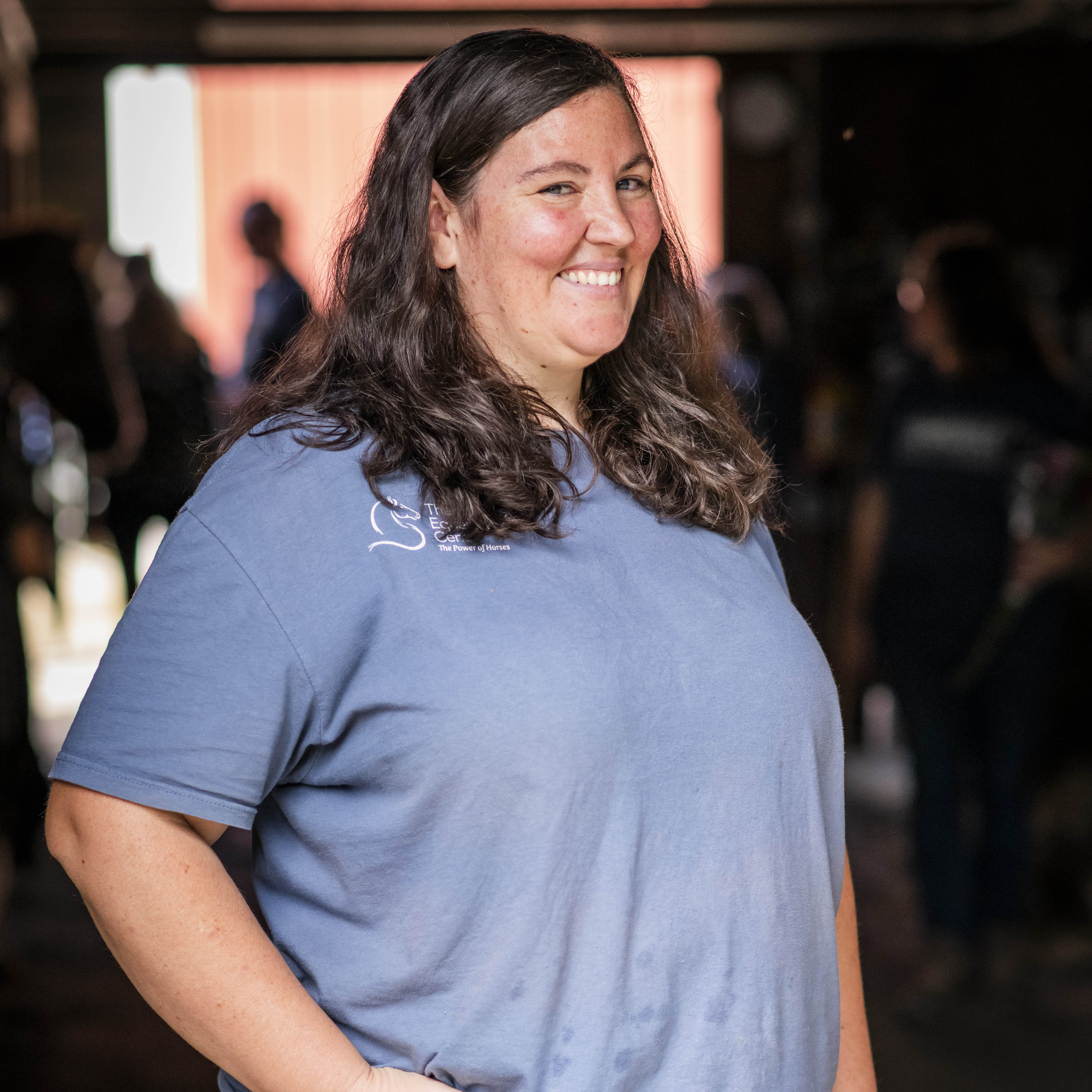 Nora Britton, barn manager and PATH certified trainer at TEC in a blue shirt in the barn.